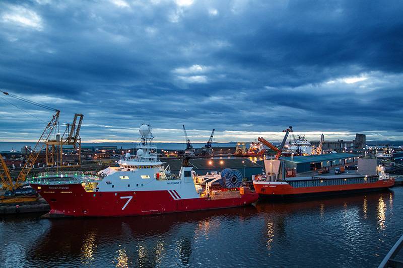 Subsea 7 vessel and red bulk vessel on harbour berth late evening at Forth Ports Leith